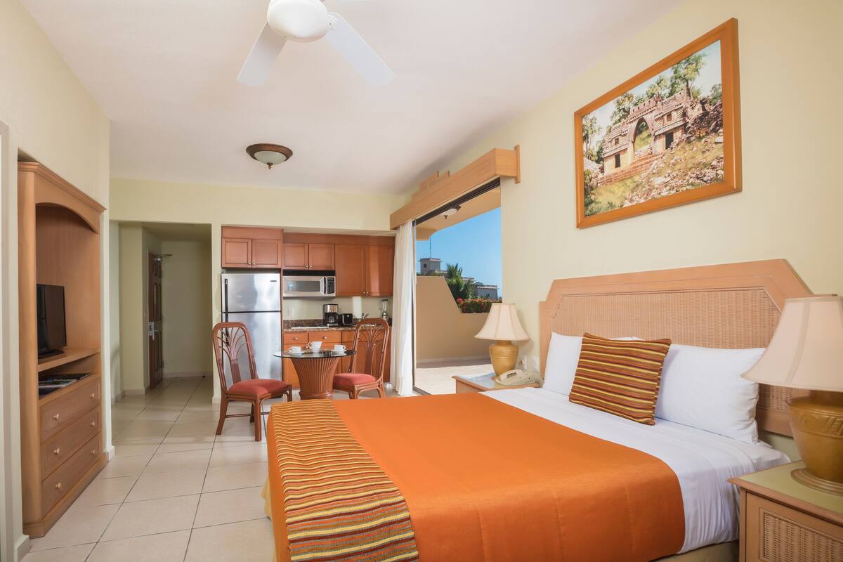 Een hotelkamer met een bed, een bureau, een stoel, een kitchenette en een balkon met uitzicht.