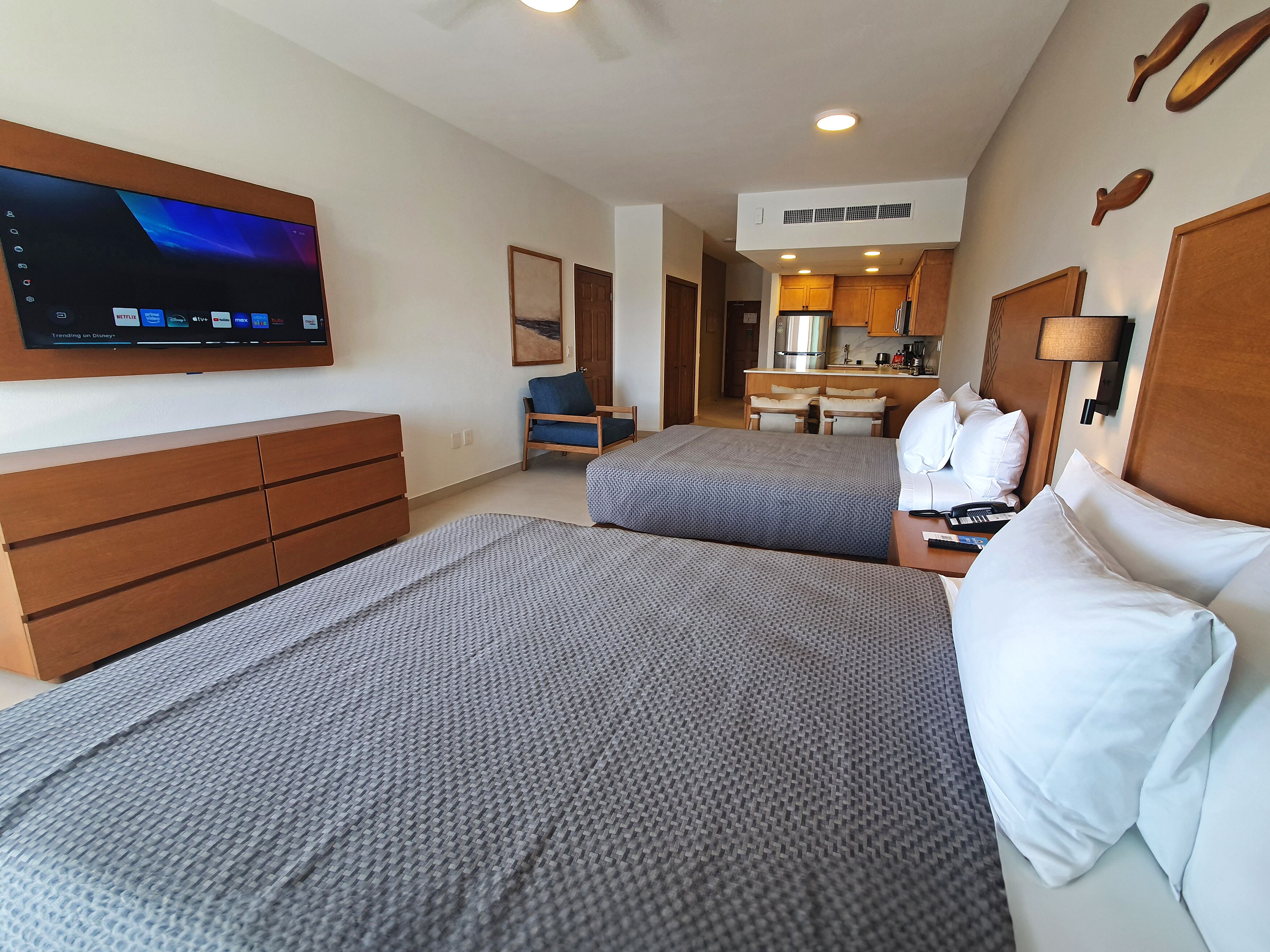 Ein Hotelzimmer mit zwei Betten, einem Fernseher, einem Schreibtisch und einer Küchenzeile.