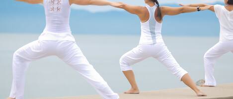 Three individuals practicing yoga on a concrete platform by a body of water.