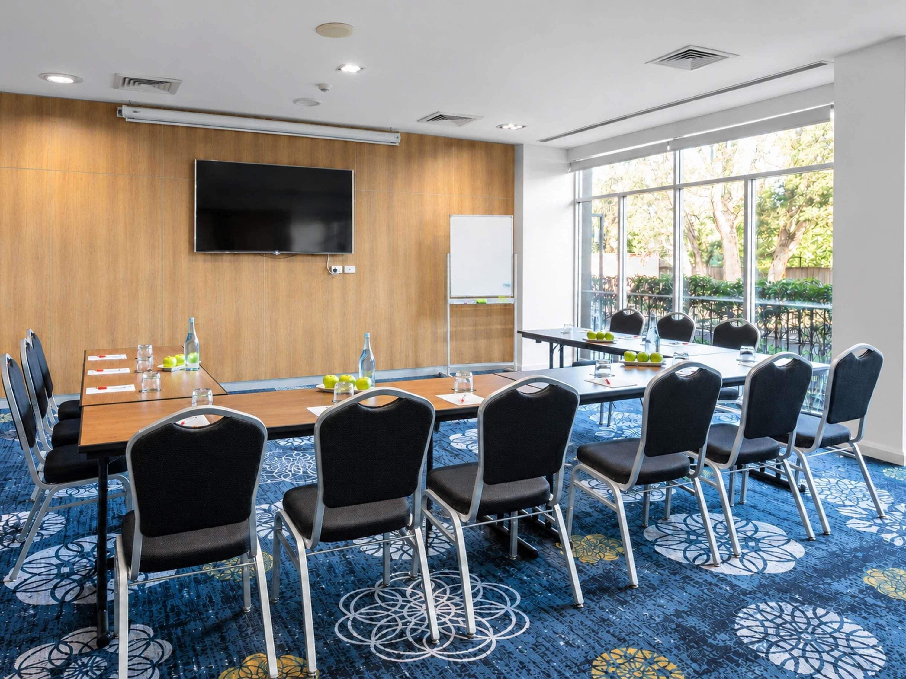 A conference room with a long table, chairs, a flat-screen TV, and a whiteboard.