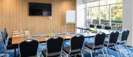 A conference room with a long table, chairs, a flat-screen TV, and a whiteboard.