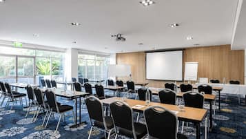 Un salón de conferencias con mesas y sillas, una pantalla de proyector y una pizarra.
