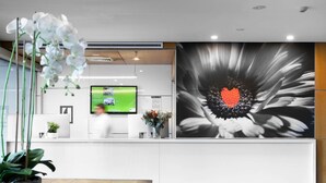 A reception desk with a digital screen, a large floral artwork, and potted plants. - Mercure Sydney St Leonards (Greenwich)