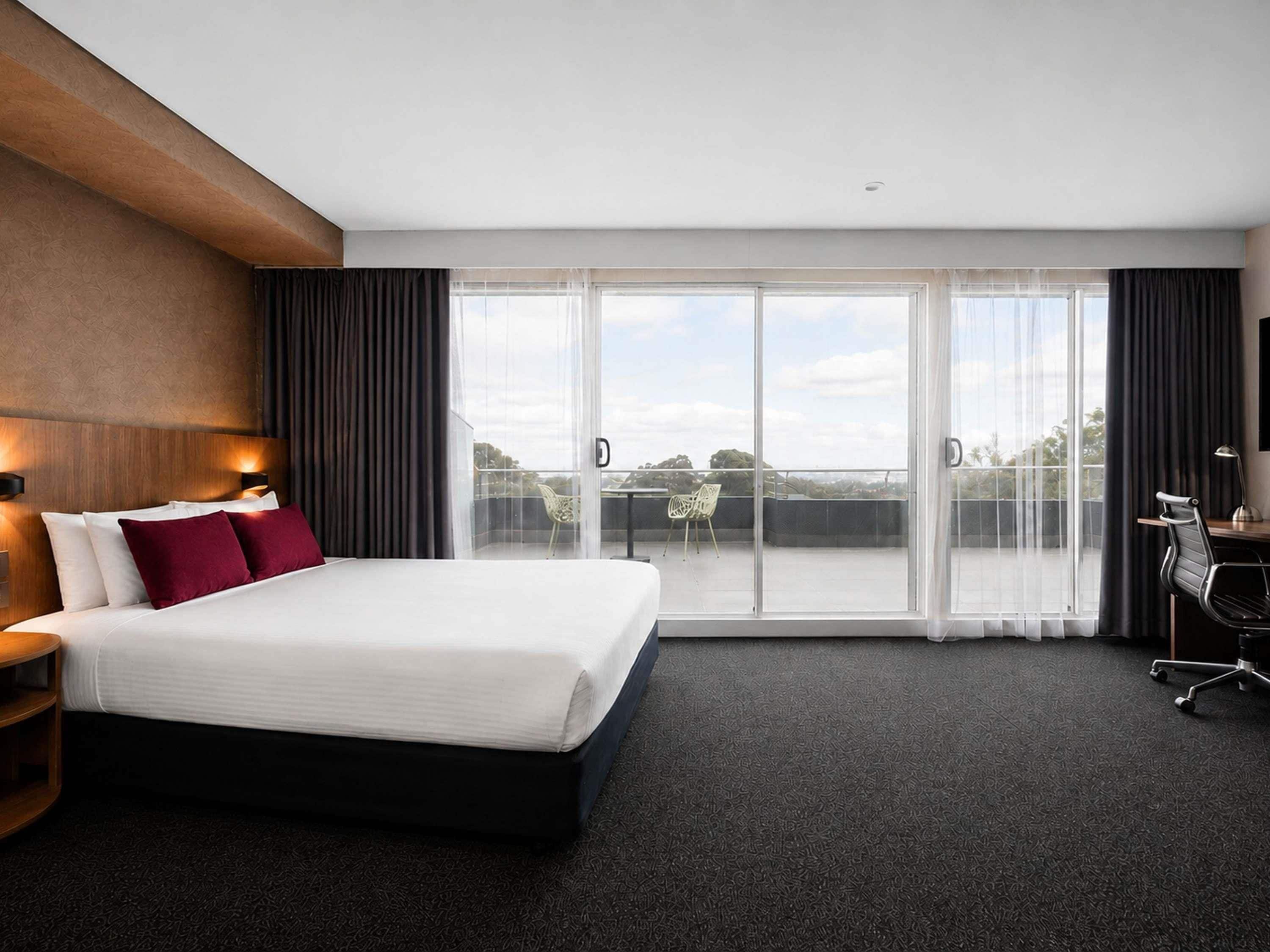 A hotel room with a large bed, a desk, a chair, and a balcony with a view.