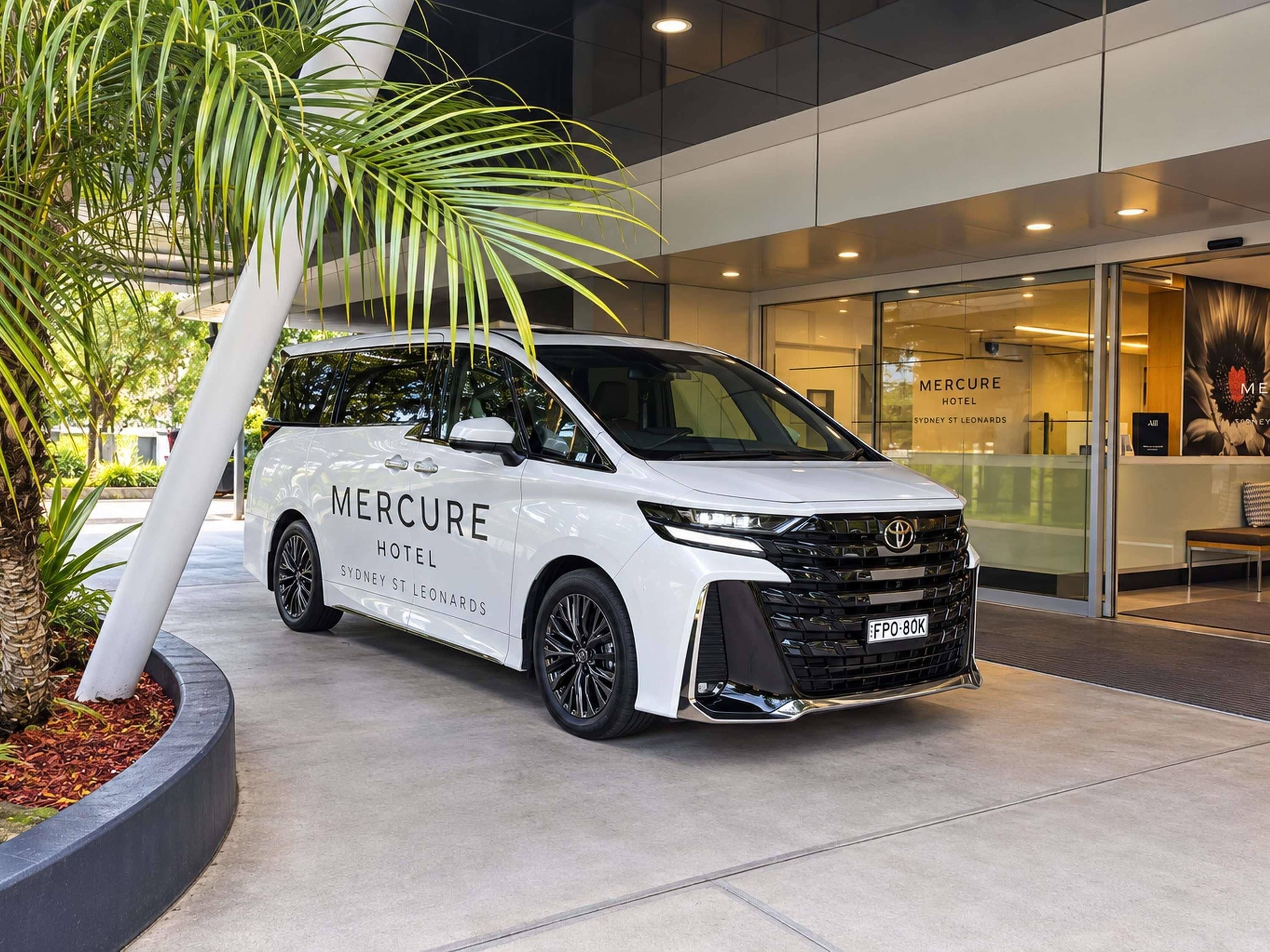 Un furgone bianco con la scritta 'Mercure Hotel Sydney St Leonards' parcheggiato di fronte a un edificio con vetrate.