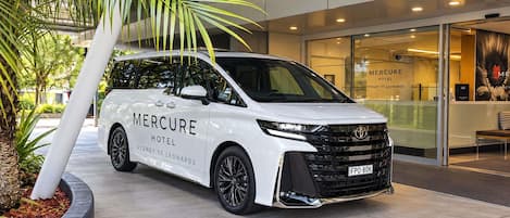 Una camioneta blanca con la publicidad del hotel 'Mercure Hotel Sydney St Leonards' estacionada frente a un edificio con puertas de vidrio.