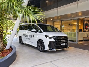 Un fourgon blanc arborant le logo « Mercure Hotel Sydney St Leonards » est garé devant un immeuble dont les portes sont en verre.