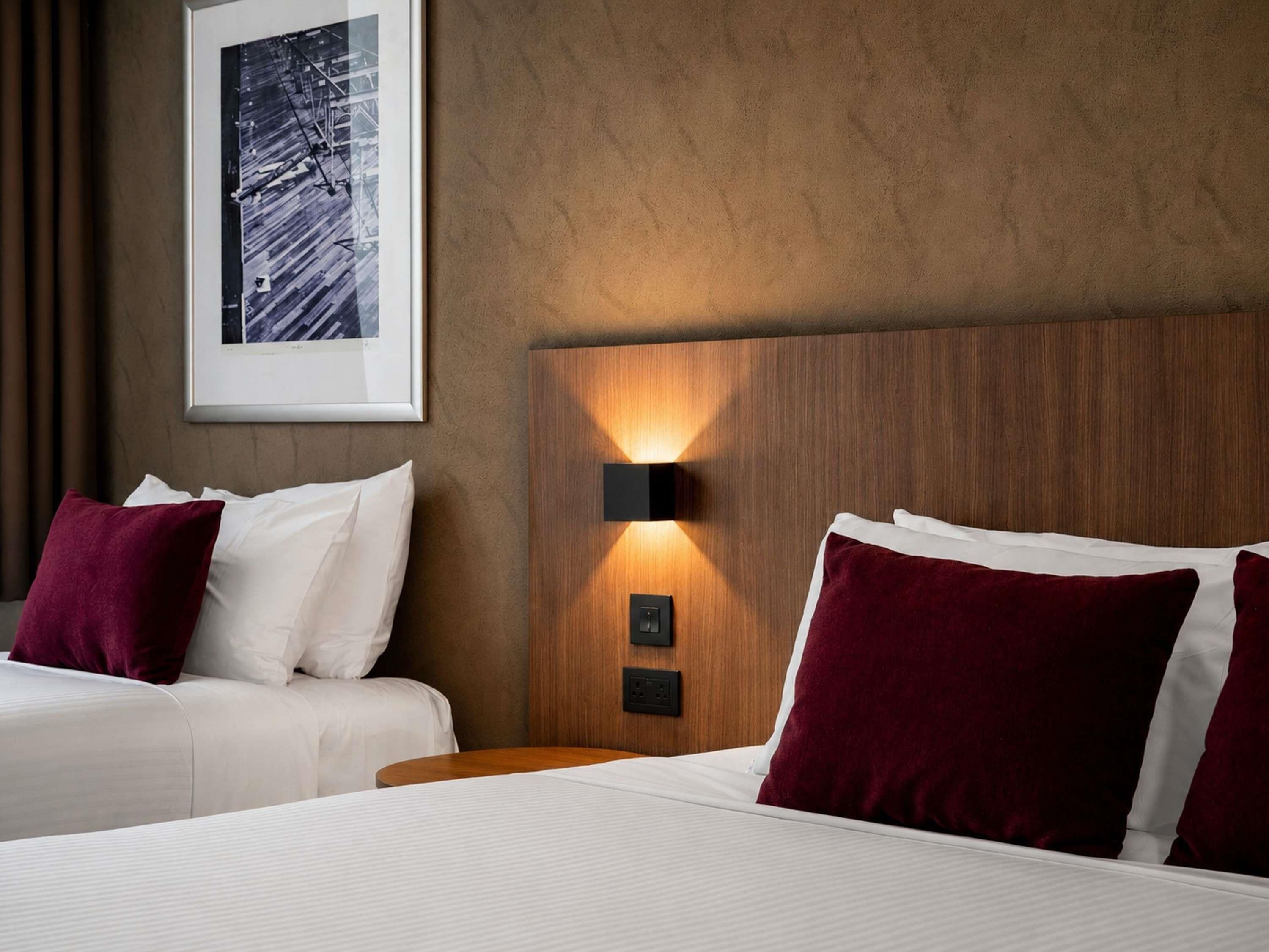 A hotel room with two beds, a framed picture on the wall, and a wall-mounted light fixture.