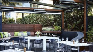 An outdoor dining area with tables and chairs, a wooden bench, and a view of greenery. - Mercure Sydney St Leonards (Greenwich)