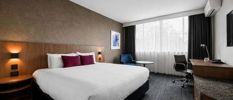 A hotel room with a large bed, bedside tables, a desk, a chair, and a window with curtains.