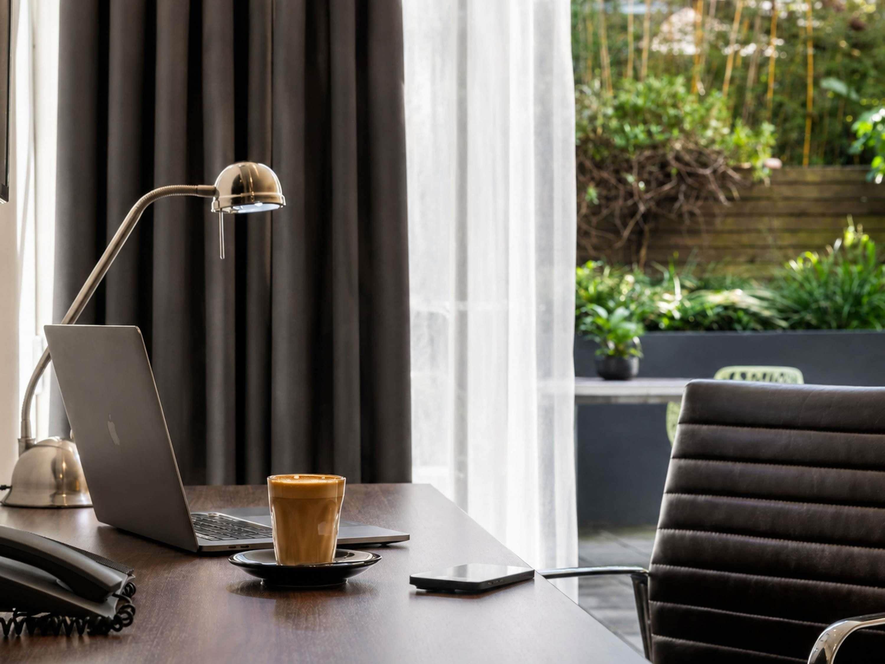 Un ordinateur portable sur un bureau, avec une tasse de café, un téléphone intelligent et un téléphone fixe.