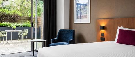 Habitación de hotel con una cama grande, una silla, una mesa y vistas a un jardín a través de una puerta corredera.