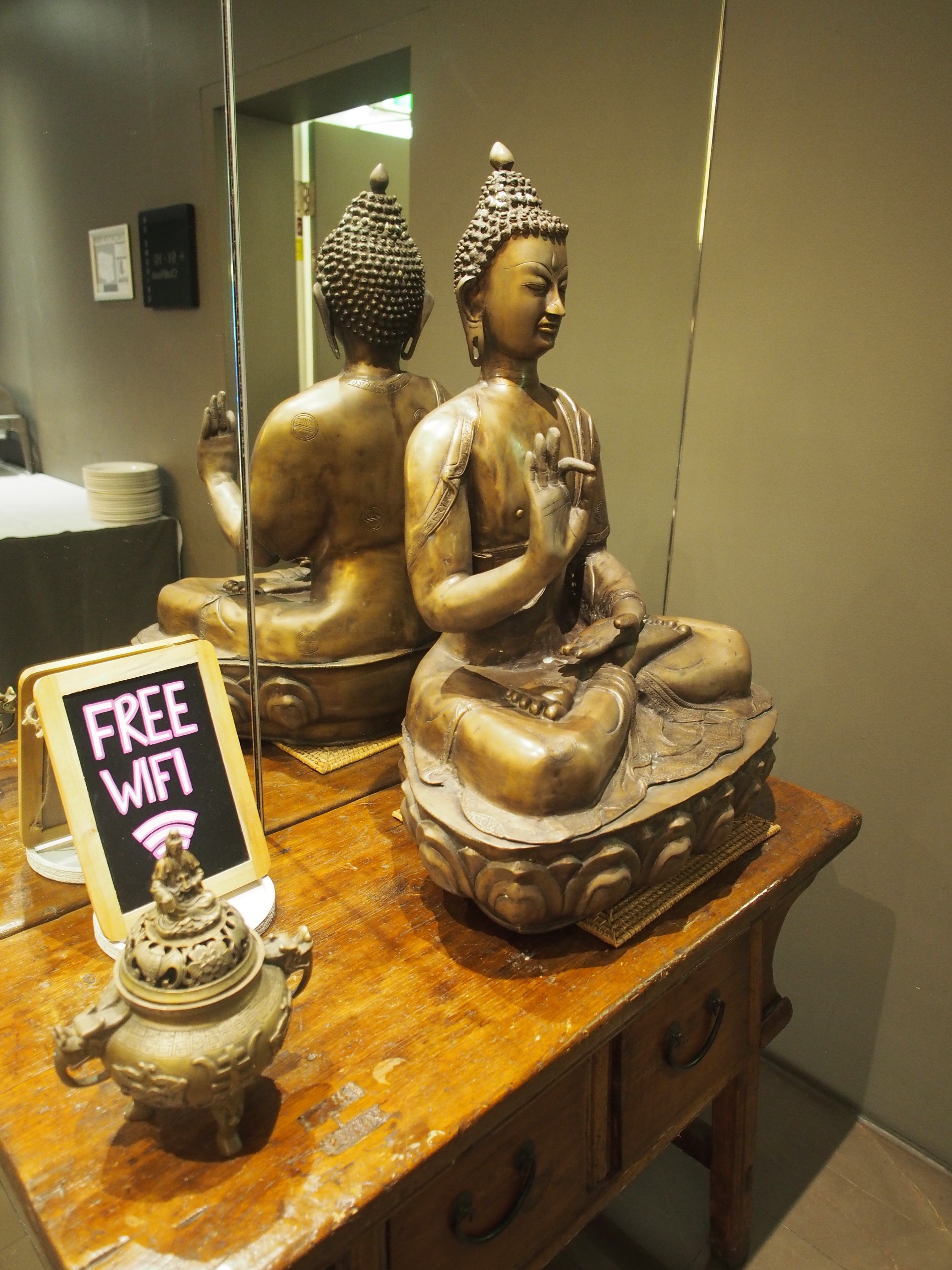 A statue of a seated figure on a wooden table with a sign indicating free wifi.