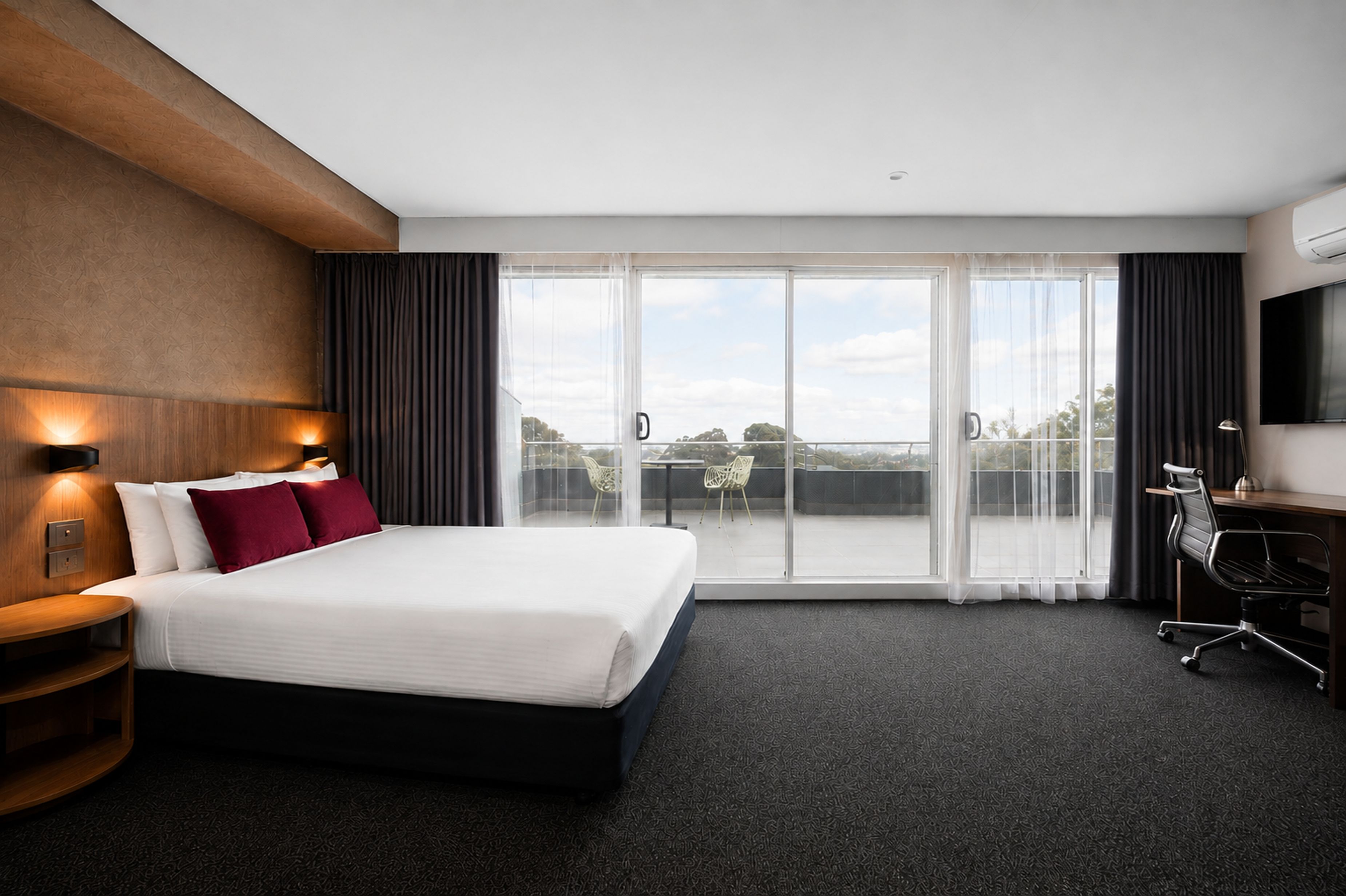 Quarto de hotel com uma cama grande, escrivaninha, cadeira, televisão e varanda com vista.