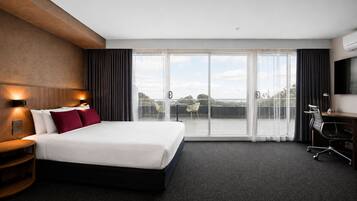 Quarto de hotel com uma cama grande, escrivaninha, cadeira, televisão e varanda com vista.