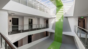 A modern building with a glass atrium, multiple floors, and a green accent wall. - Mercure Sydney St Leonards (Greenwich)