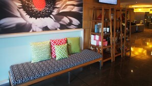 A lobby with a bench, a wall-mounted TV, and a shelf with various items. - Mercure Sydney St Leonards (Greenwich)