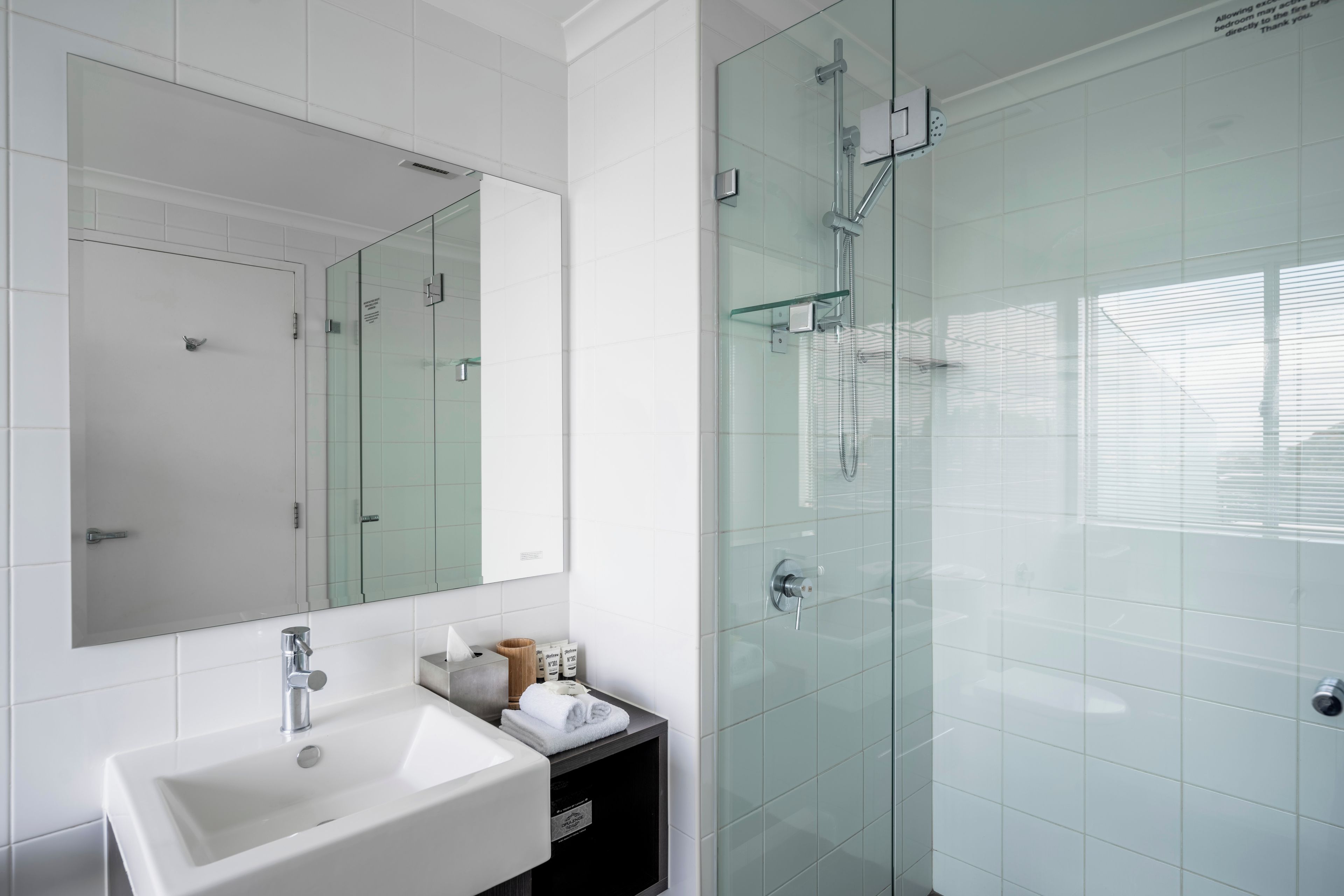 Un baño moderno con un lavamanos blanco, un espejo y una ducha con cerramiento de vidrio.