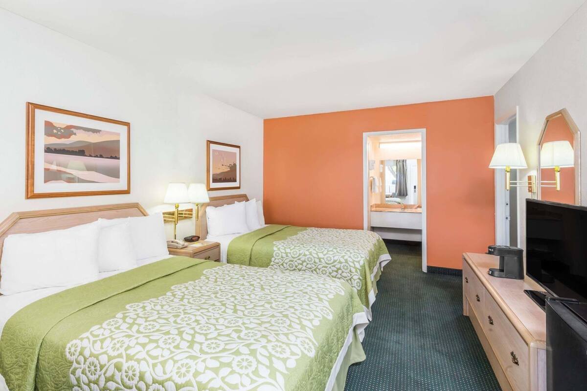 Une chambre d’hôtel avec deux lits, une télévision, une commode et deux lampes.