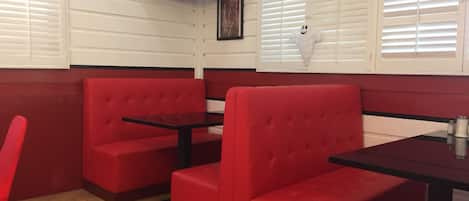 A restaurant interior with red booths and black tables, a television mounted on the wall, and white blinds on the windows.