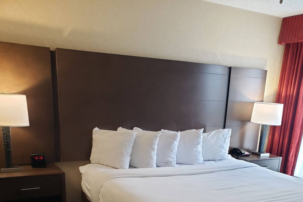 A hotel room with a large bed, two bedside tables, a nightstand, a clock, and a telephone.