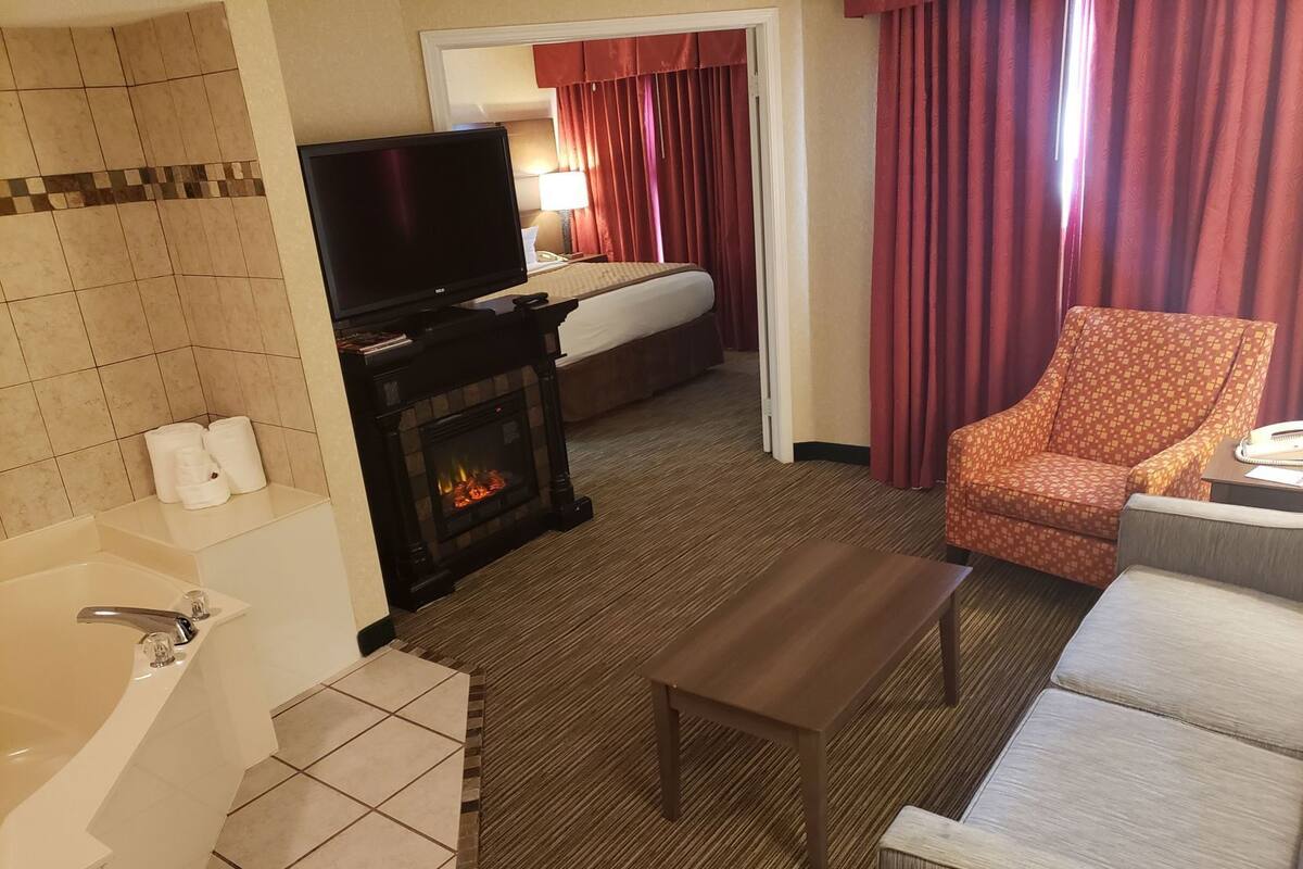 A hotel room with a fireplace, a television, a sofa, a chair, and a bed.
