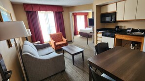 Une chambre d’hôtel équipée d’un canapé, d’un fauteuil, d’une table à manger, d’une kitchenette et donnant sur la chambre voisine.