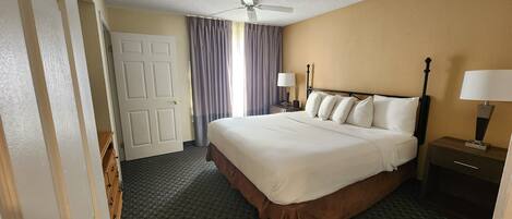 Une chambre d’hôtel avec un lit, une table de chevet avec une lampe, un ventilateur de plafond et une porte.