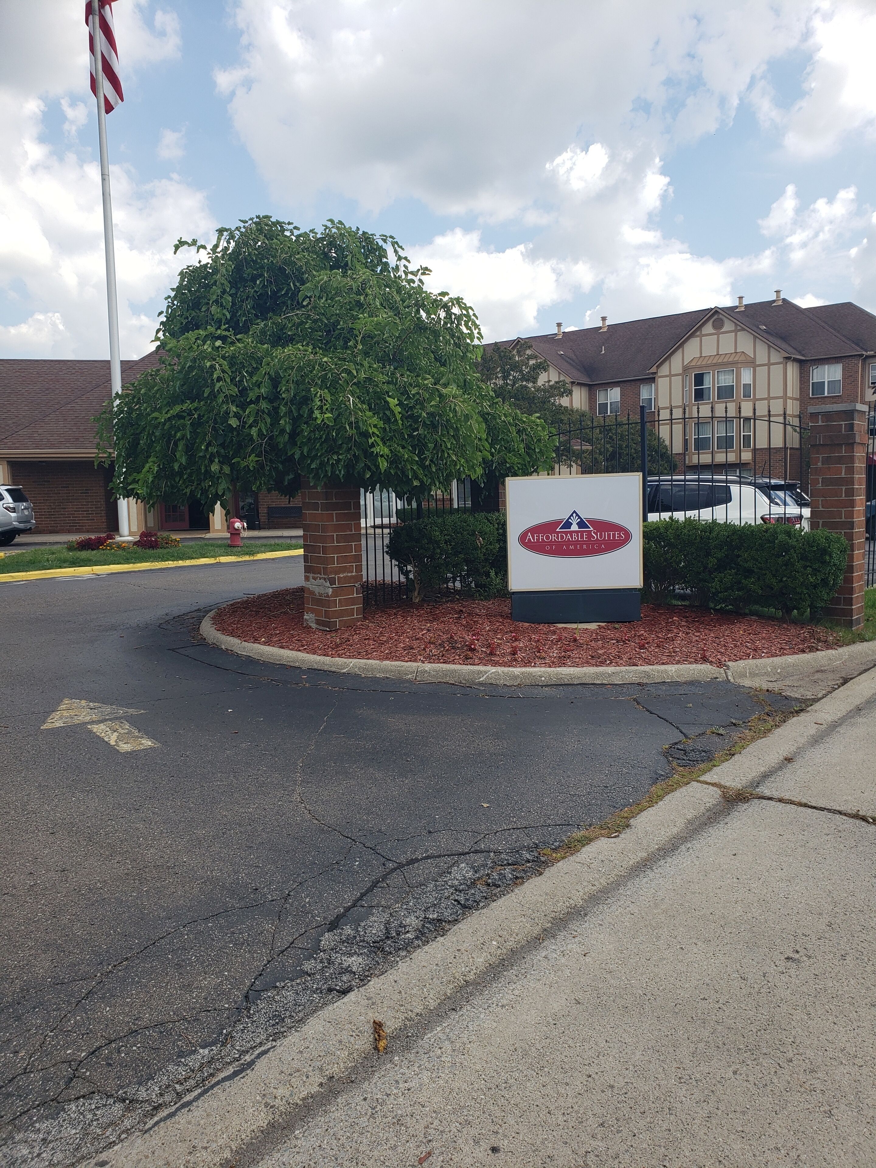 A hotel entrance with a sign for Affordable Suites of America, a brick building, and a flagpole.