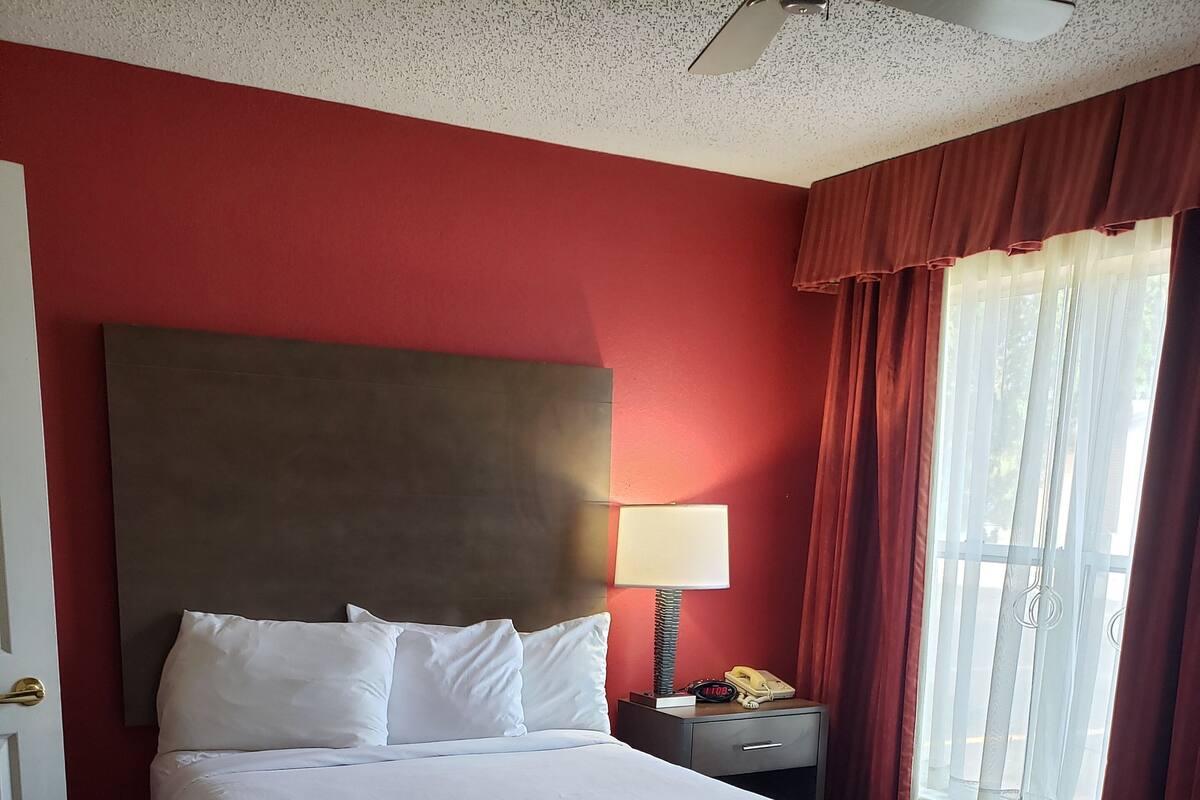 A hotel room with a large bed, a nightstand, a lamp, a telephone, and a window with curtains.