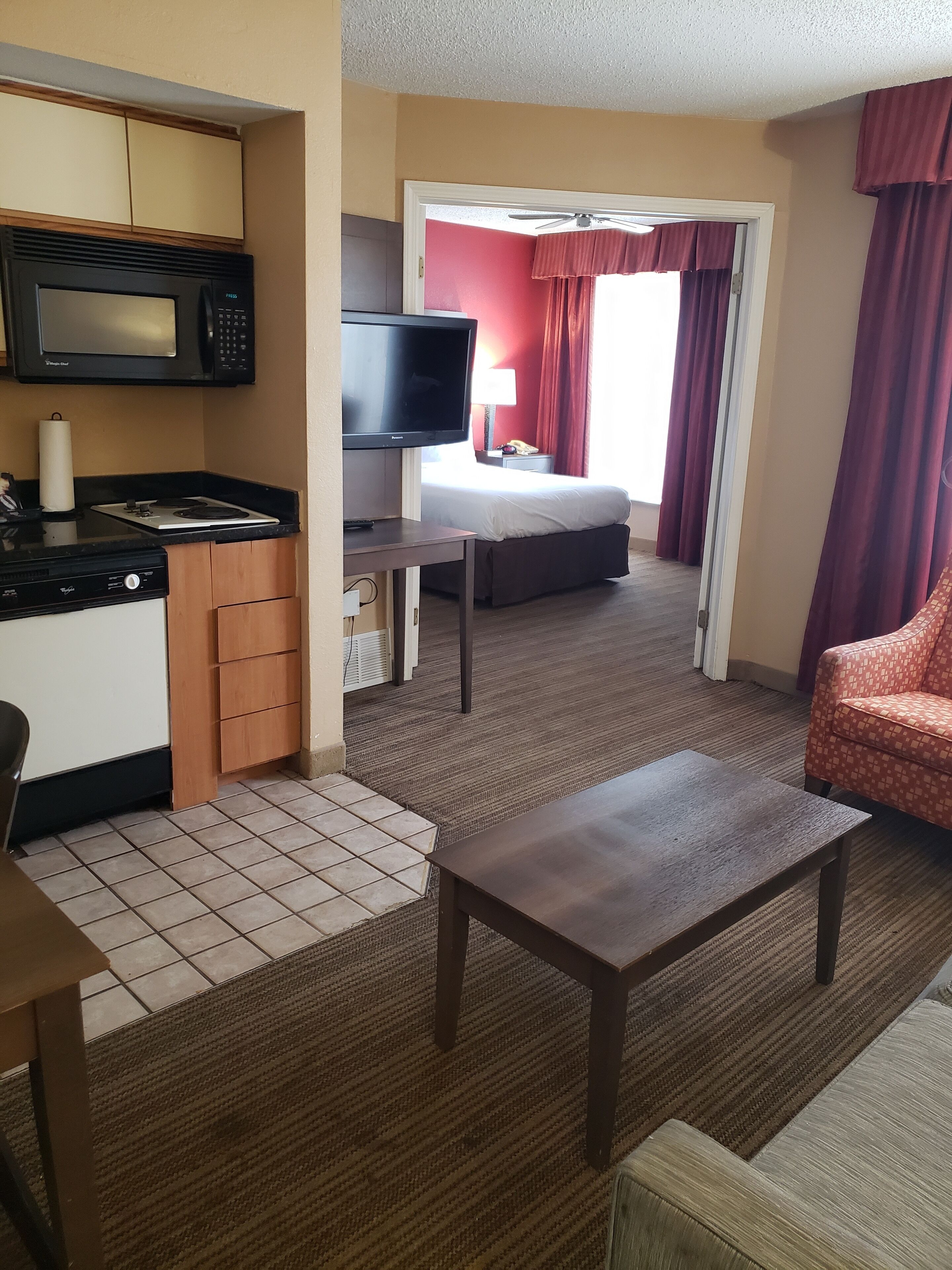 A compact hotel room with a kitchenette, a television, a bed, and a seating area.