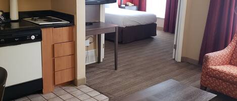 A compact hotel room with a kitchenette, a television, a bed, and a seating area.