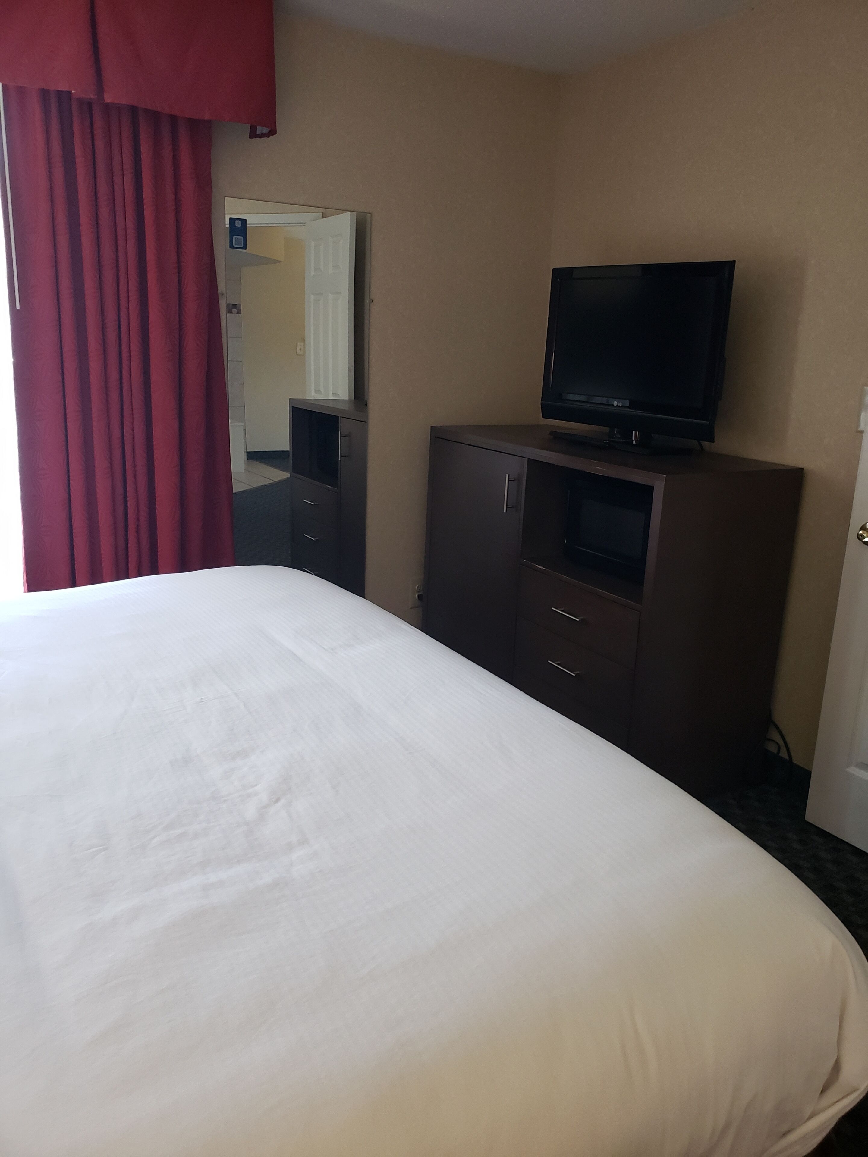 A hotel room with a bed, a television on a cabinet, a mirror, and a door.