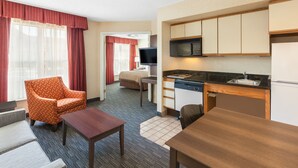Une chambre d’hôtel équipée d’une kitchenette, d’un canapé, d’un fauteuil, d’une petite table et d’un téléviseur.