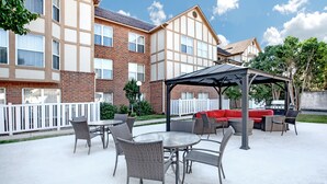 Un espace patio aménagé avec du mobilier d’extérieur, un coin salon abrité et un bâtiment en briques en arrière-plan.