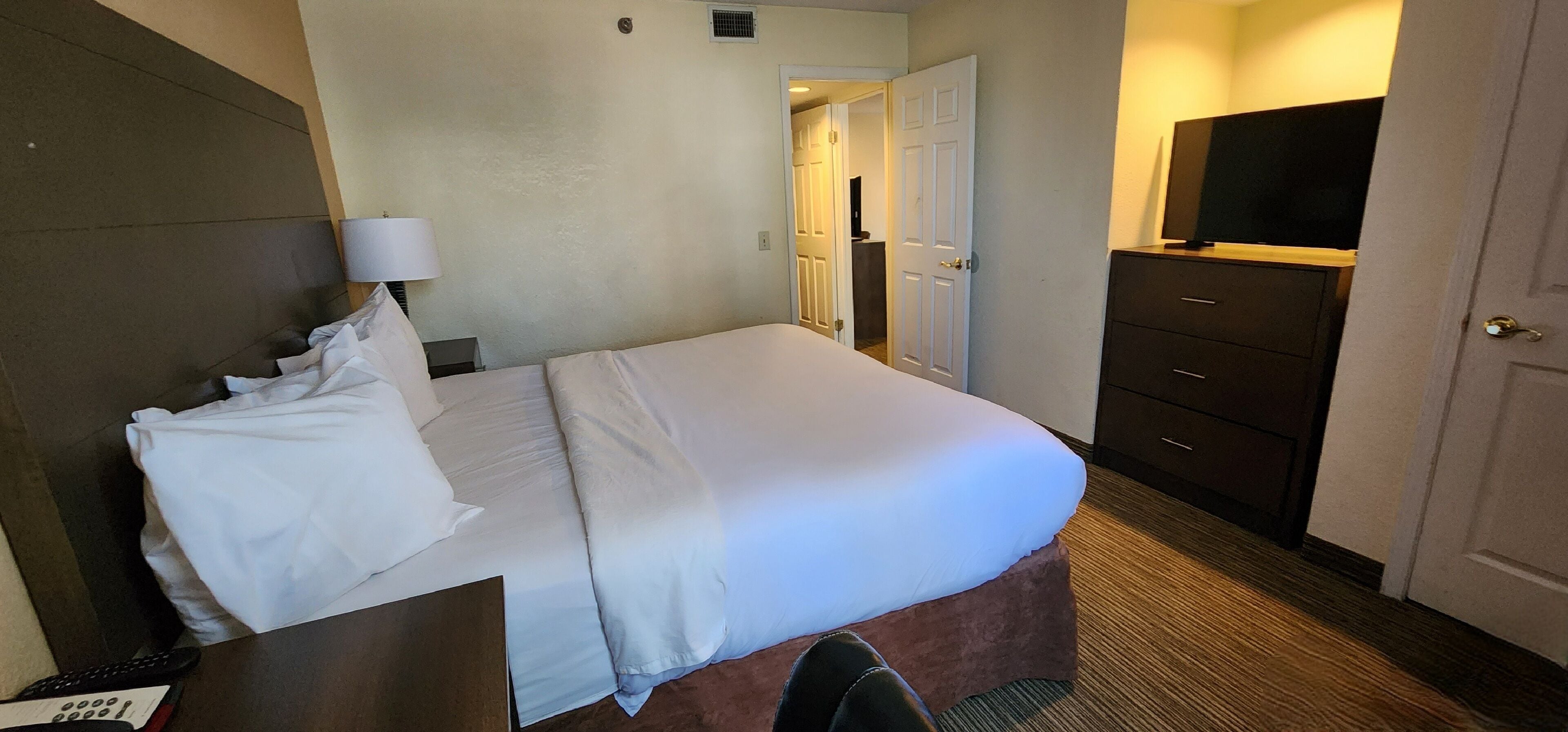 A hotel room with a bed, a desk with a lamp, a dresser, and a television.