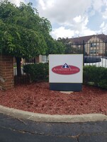 A sign for Affordable Suites of America with a brick pillar and mulch ground cover.