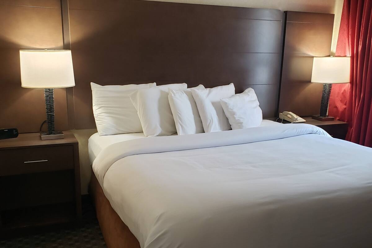 A hotel room with a large bed, two bedside tables with lamps, a telephone, and a red curtain.