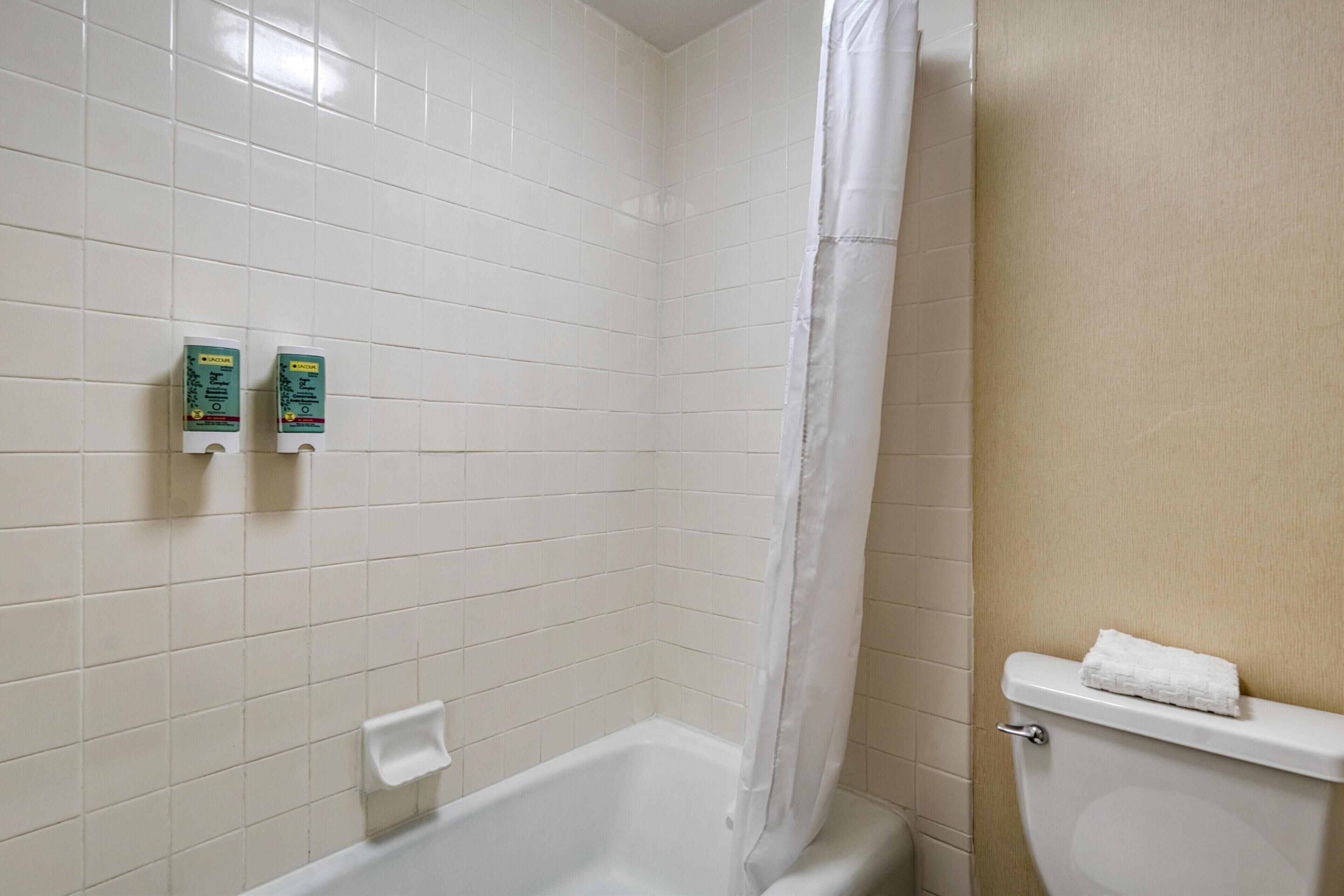 A bathroom with white tiled walls, a bathtub, a toilet, and two boxes of hand soap on the wall.