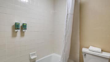 A bathroom with white tiled walls, a bathtub, a toilet, and two boxes of hand soap on the wall.
