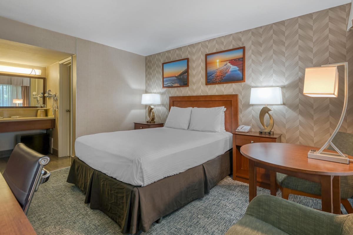 Ein Hotelzimmer mit einem großen Bett, zwei Nachttischen mit Lampen, einem Schreibtisch, einem Stuhl und einem kleinen runden Tisch.