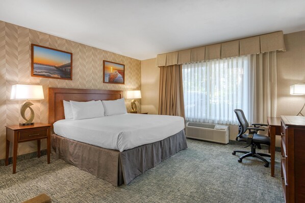 Une chambre d’hôtel avec un grand lit, deux tables de chevet avec des lampes, un bureau avec une chaise et une grande fenêtre avec des rideaux.