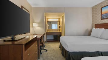 Une chambre d’hôtel avec un lit, un bureau avec une télévision, une commode, un miroir et une salle de bain visible à travers une porte ouverte.