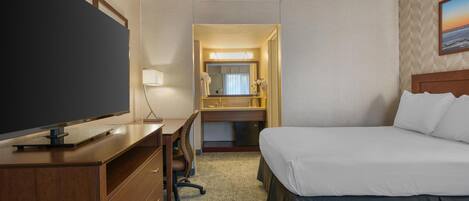 A hotel room with a bed, a desk with a TV, a dresser, a mirror, and a bathroom visible through an open door.