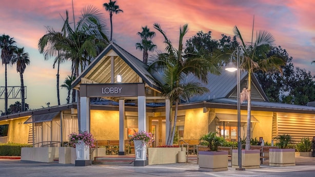 Hall d'albergo con un cartello 'Lobby', palme e cielo al tramonto.