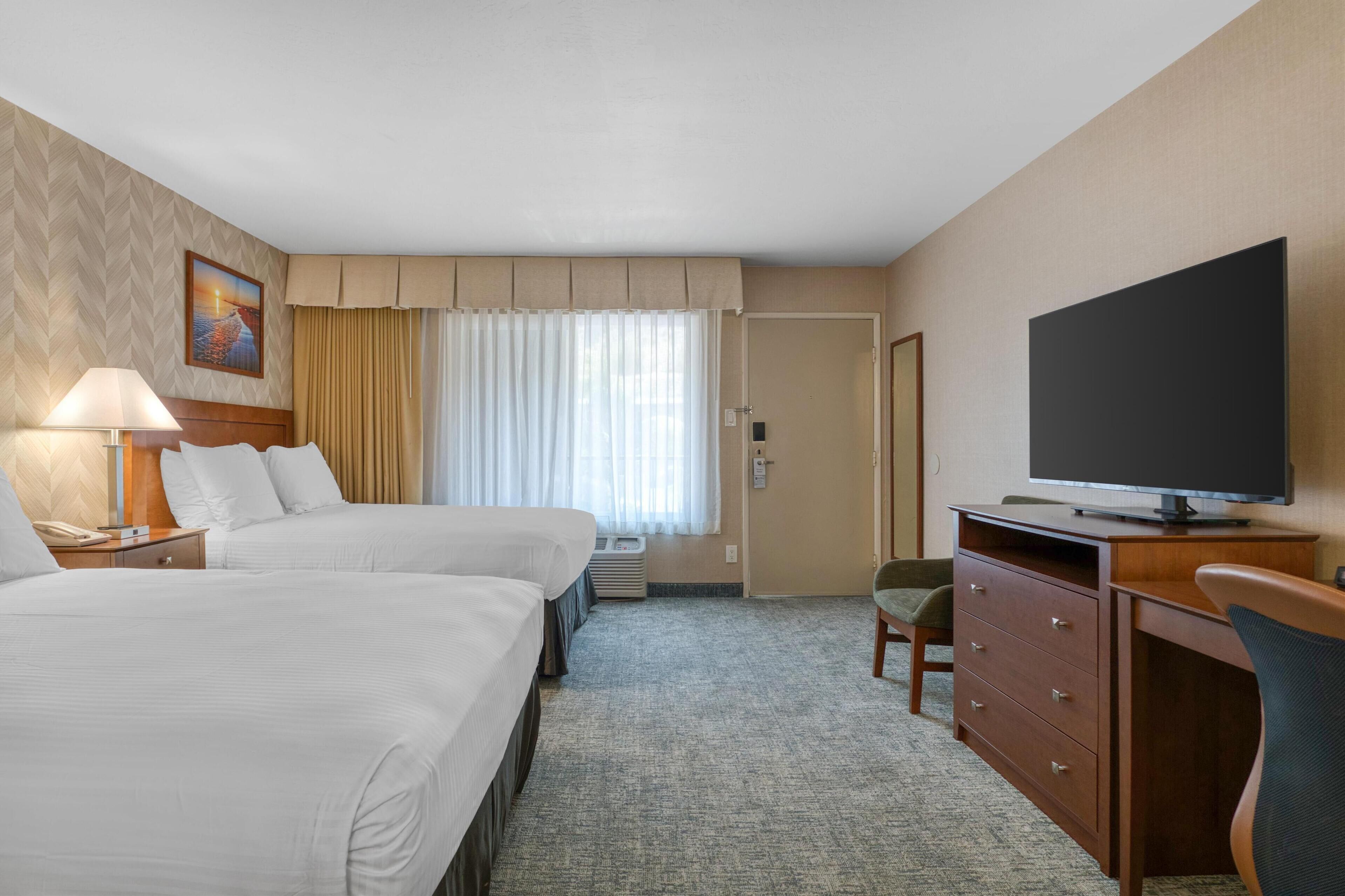 Habitación de hotel con dos camas, un escritorio, un televisor y una silla.