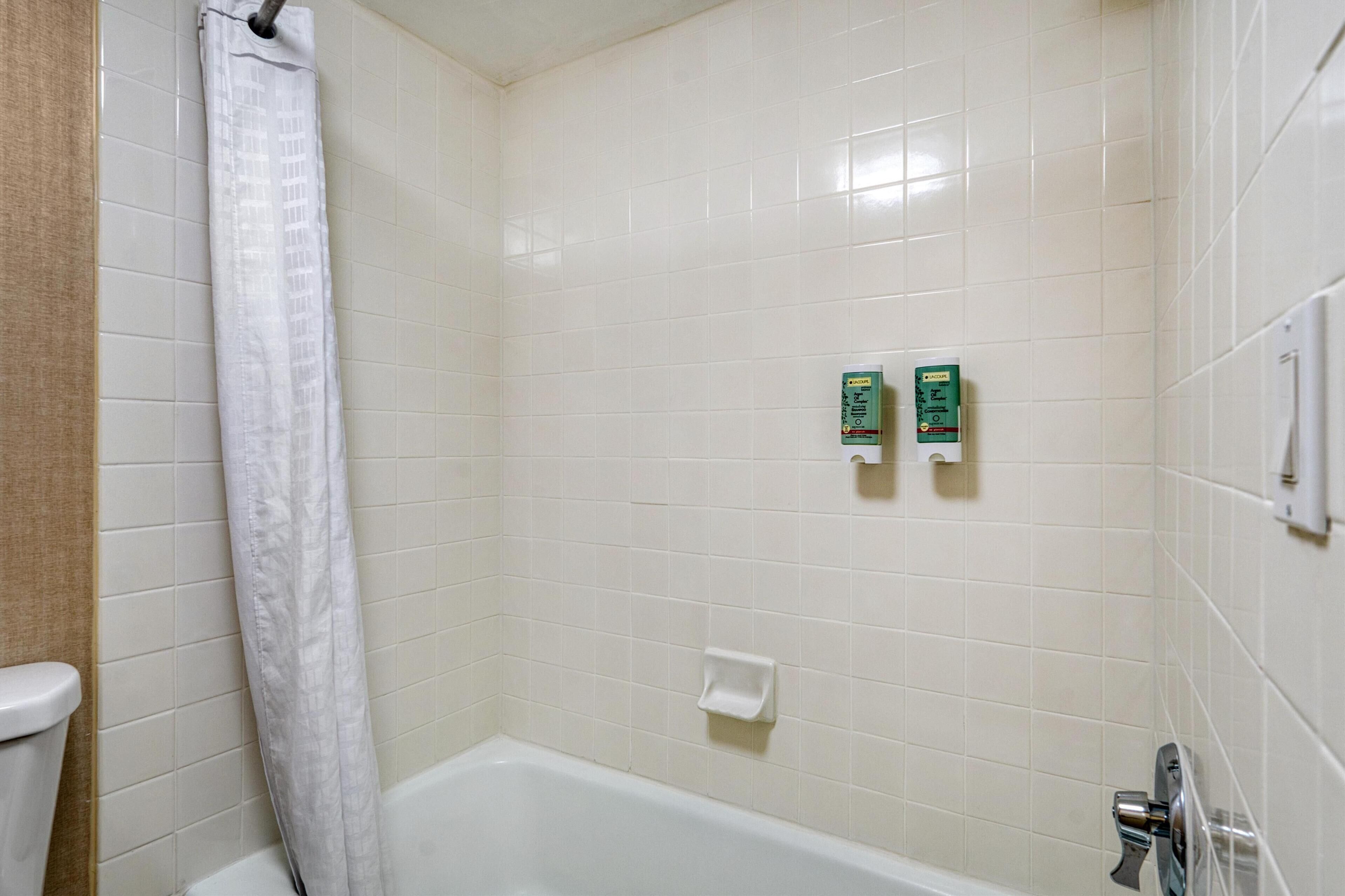 A bathroom with a bathtub, a toilet, and a shower curtain. There are two soap dispensers on the wall.