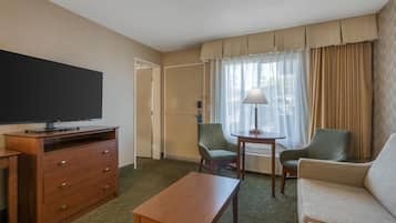 Una habitación de hotel con televisión de pantalla plana, cómoda de madera, una mesita, dos sillones y un sofá.