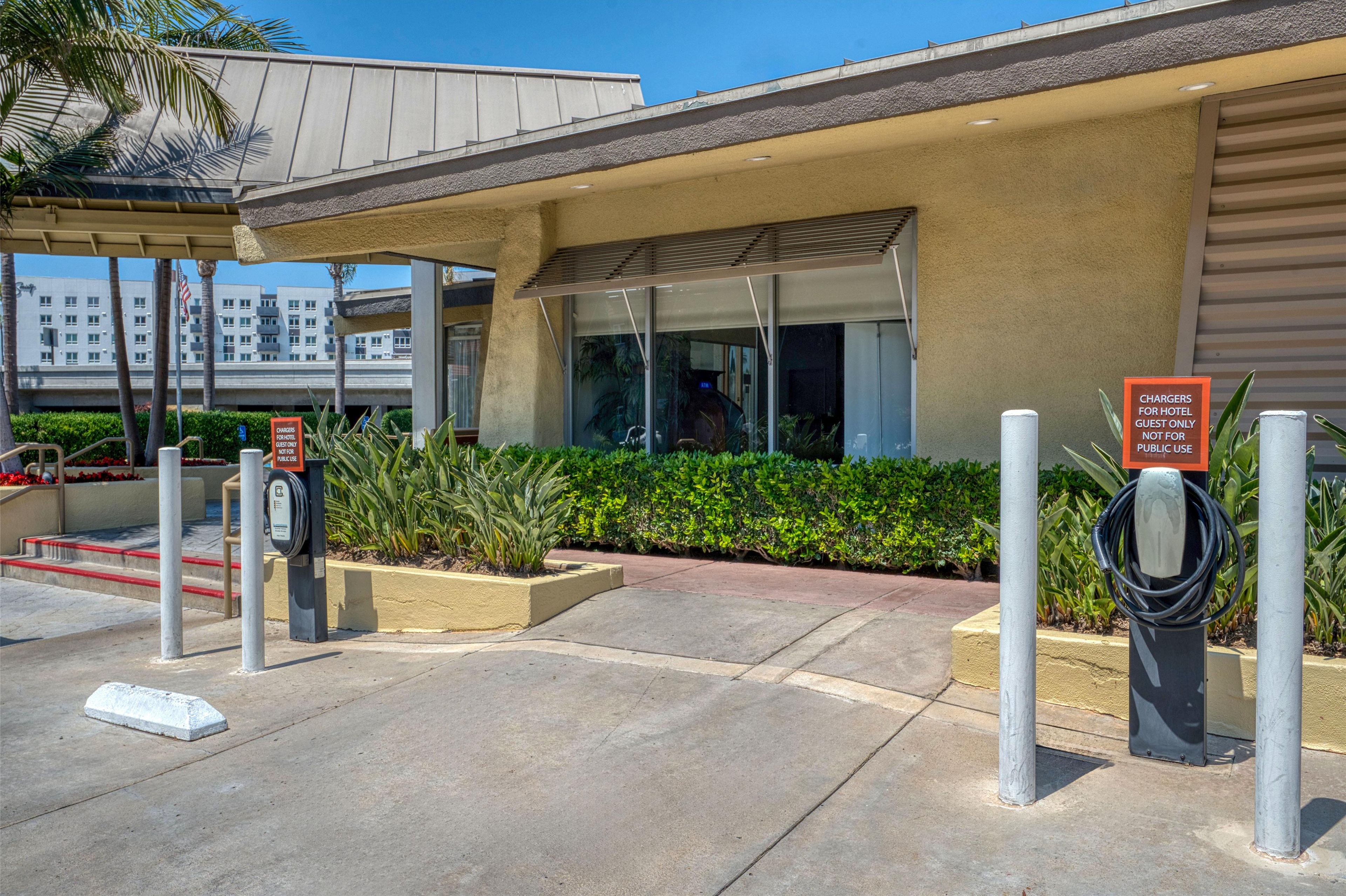 A hotel entrance with a covered walkway, a parking area, and a sign indicating chargers for hotel guests only.