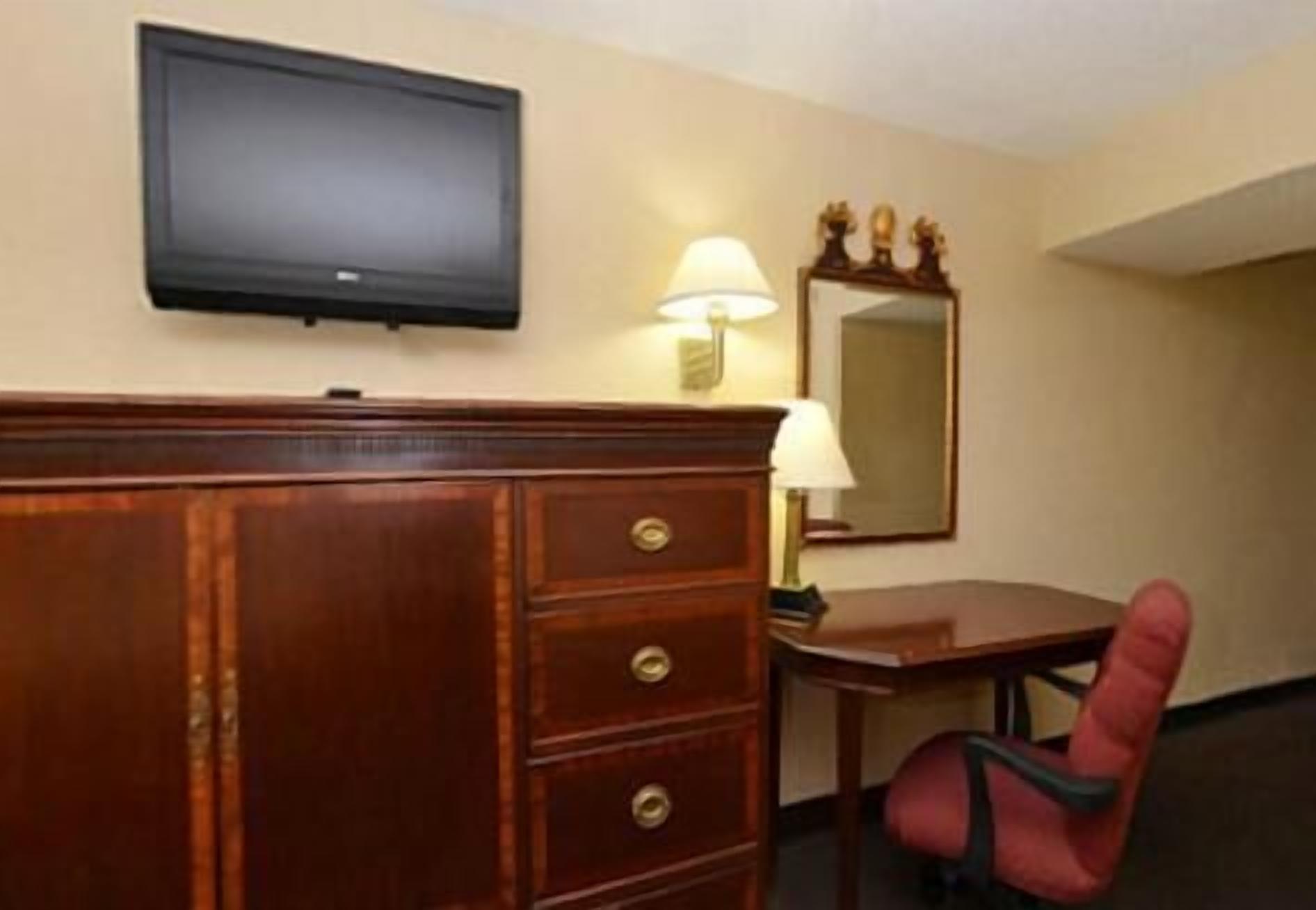 Een hotelkamer met een houten dressoir, een bureau, een stoel, een wandtelevisie en een spiegel.